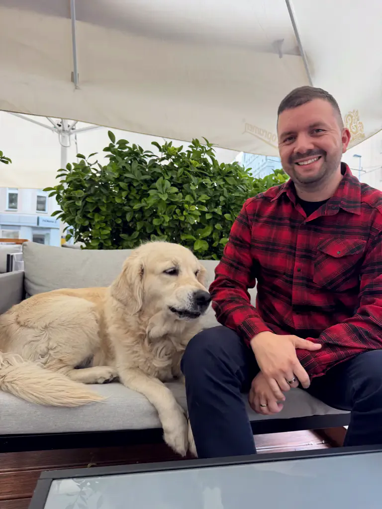 O Peter sentado na esplanada a sorrir, ao lado dele está deitada a Tiffany, uma golden retriever